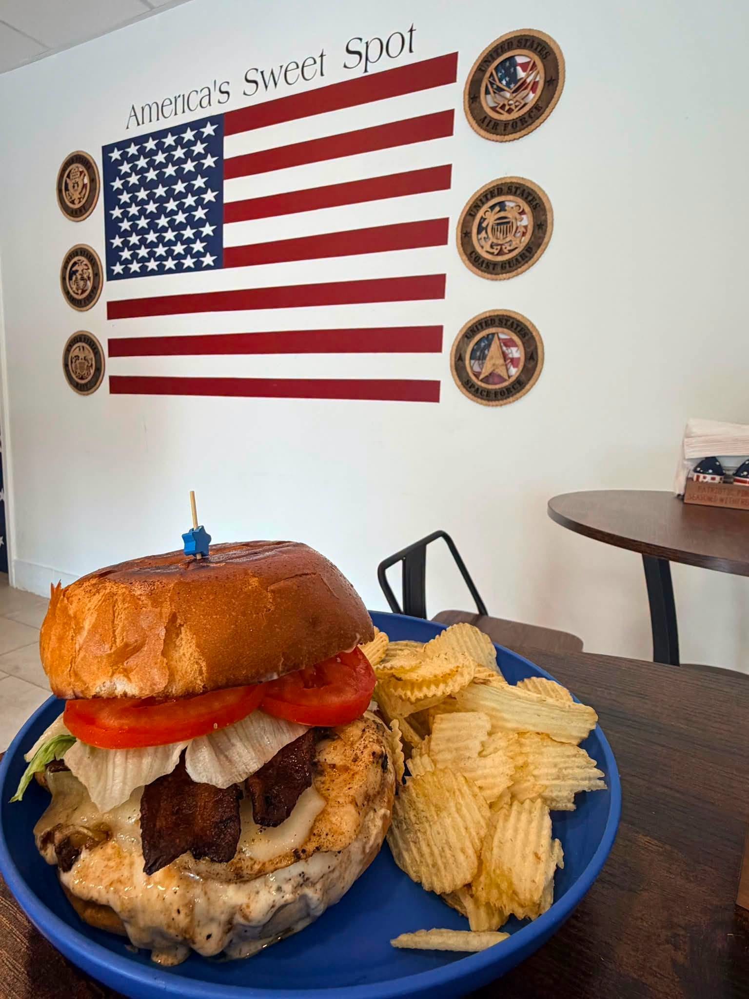 Bacon cheeseburger with tomato and lettuce next to a pile of chips