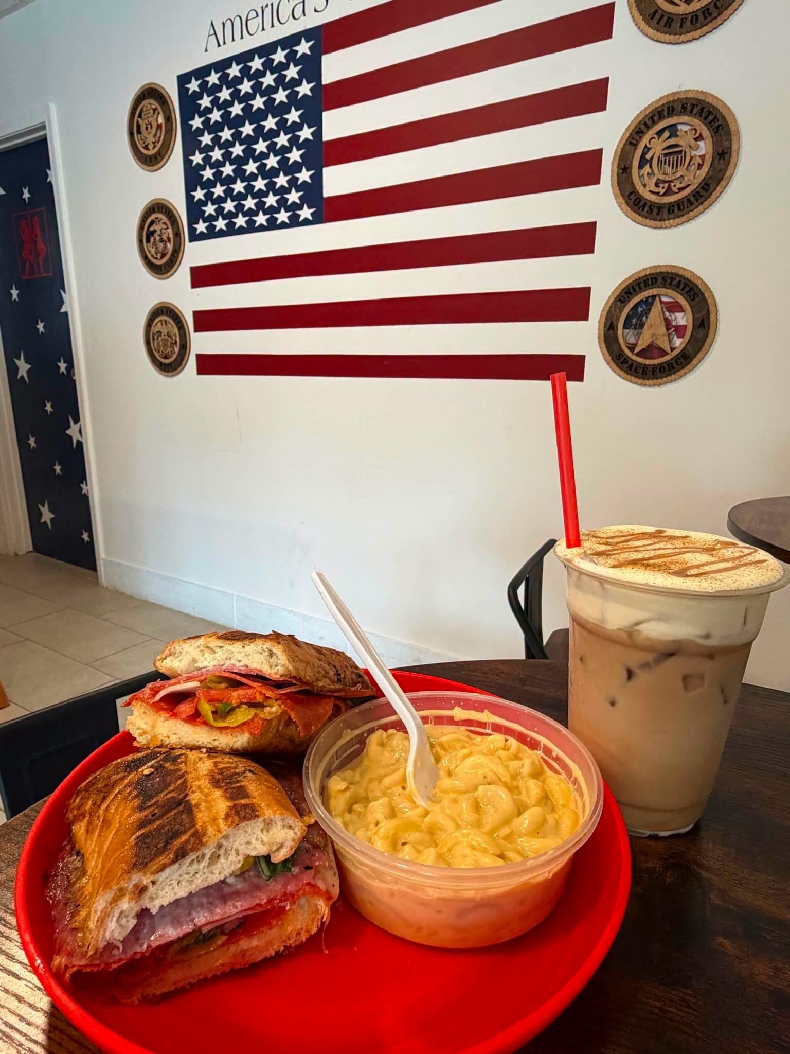 Sandwich, mac and cheese cup and iced coffee in front of the flag wall